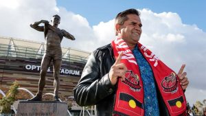 Former St Kilda champion Nicky Winmar standing right infront of his statue at Optus Stadium. 