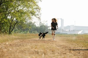 Cheerful woman running with Collie dog in nature