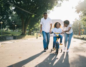 parents teaching little girl how to ride a bike